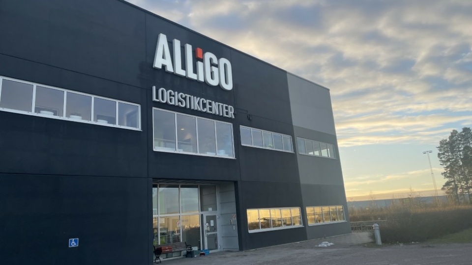 Alligo logistics center building with logo, large windows, and sunset in the background