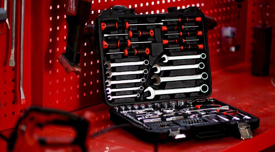 Open tool case with wrenches and screwdrivers on red workbench