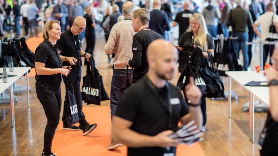 Alligo staff welcoming guests and handing out bags at a crowded event