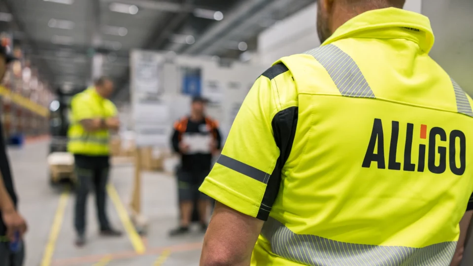 Alligo worker in hi-vis yellow shirt seen from behind in a warehouse environment