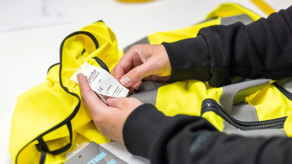 Hands holding and inspecting label inside a yellow high-visibility jacket