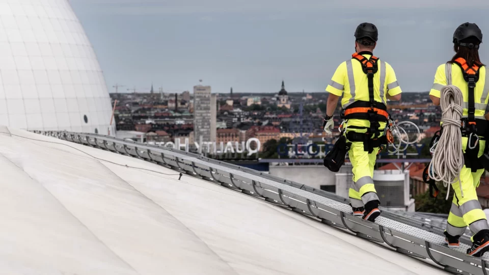 Two workers in safety gear walking on a rooftop with cityscape in the background