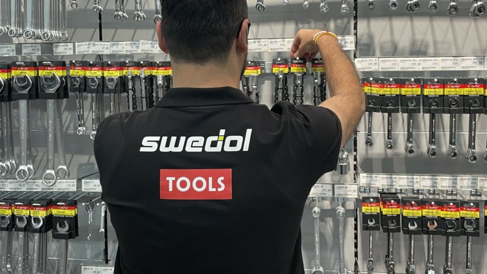 A person in a Swedol shirt organizing wrenches on a tool wall