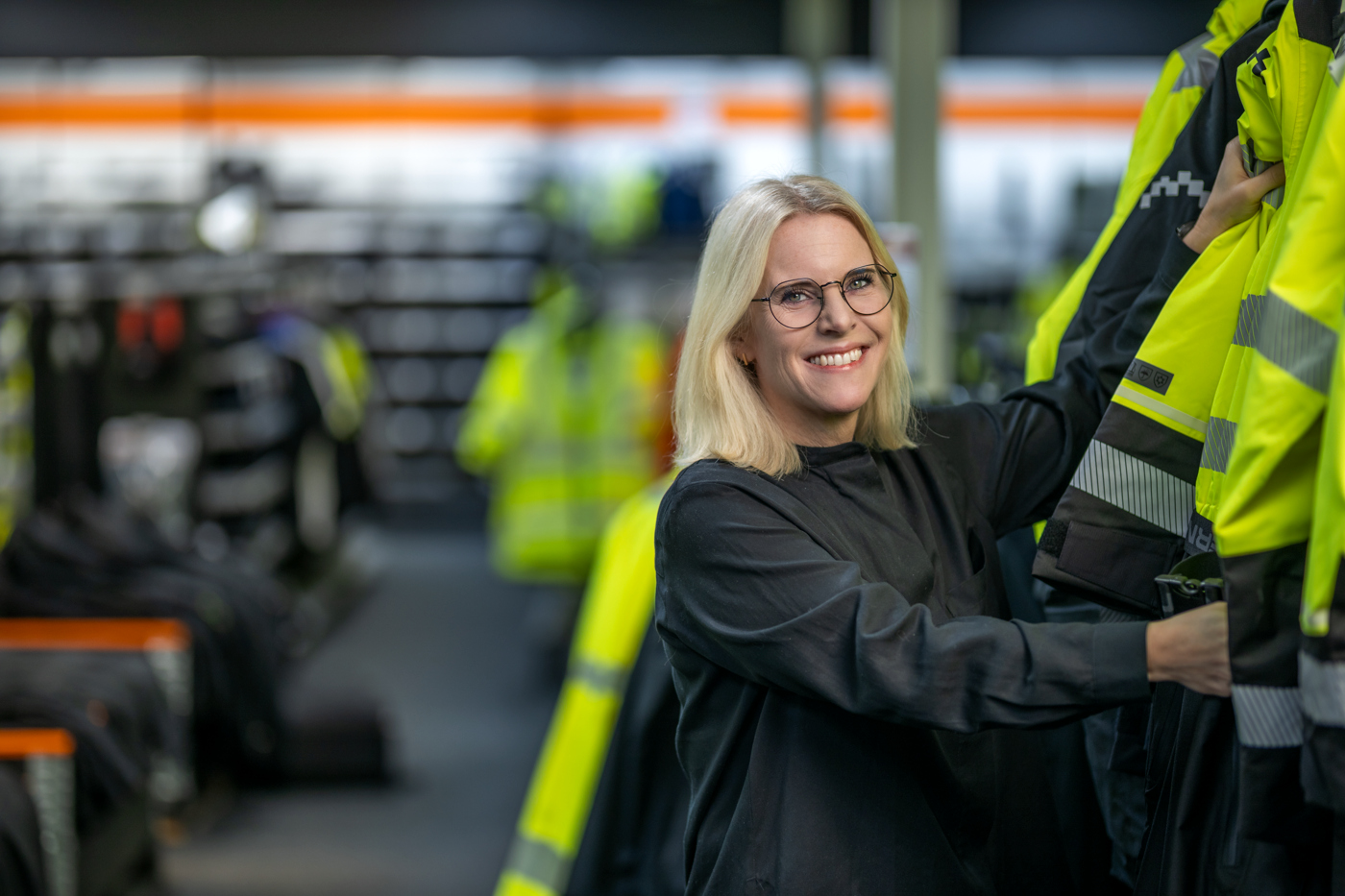 Smiling woman arranging high-visibility work jackets in a store