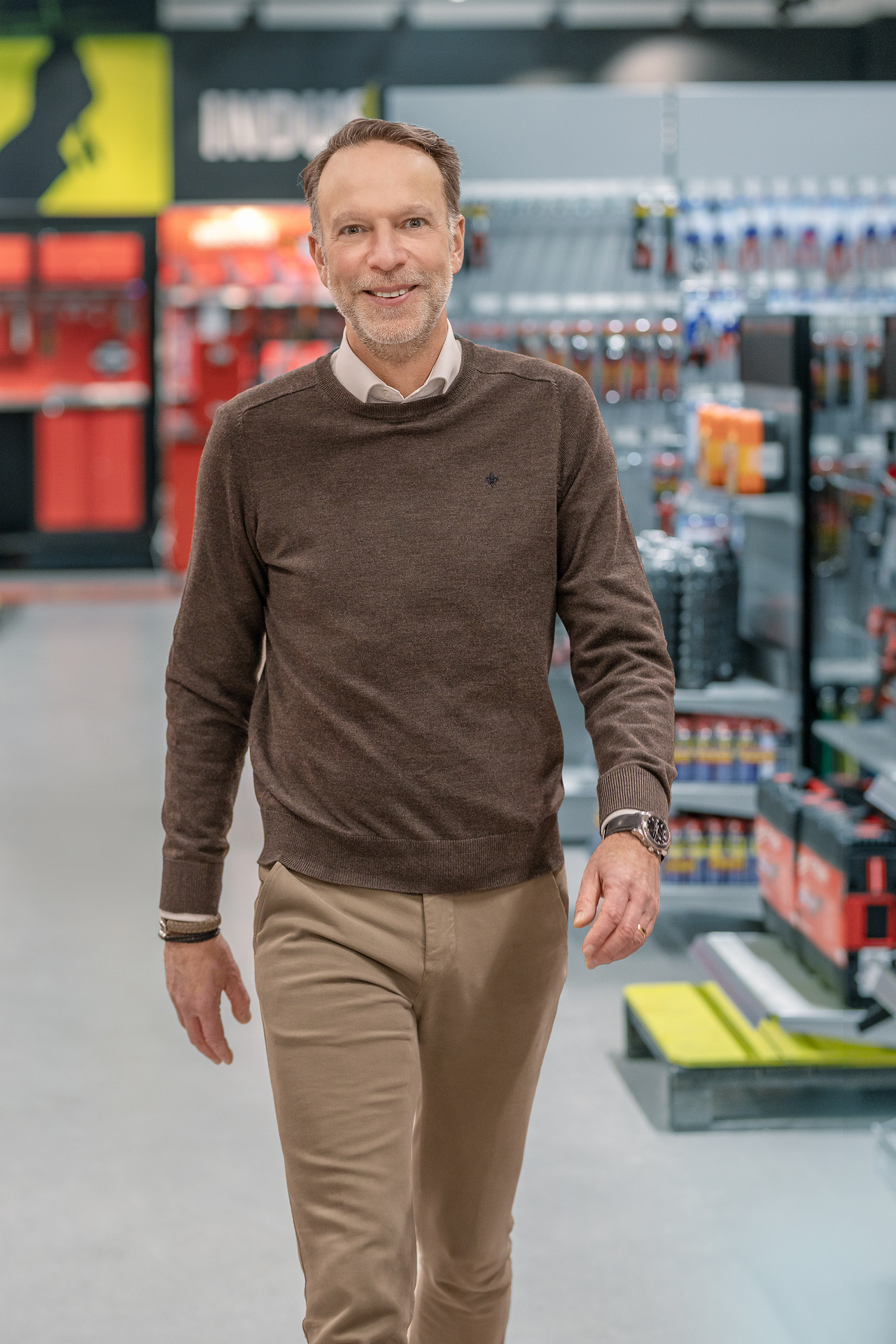 Leende man går genom en verktygsbutik i brun tröja och beiga byxor