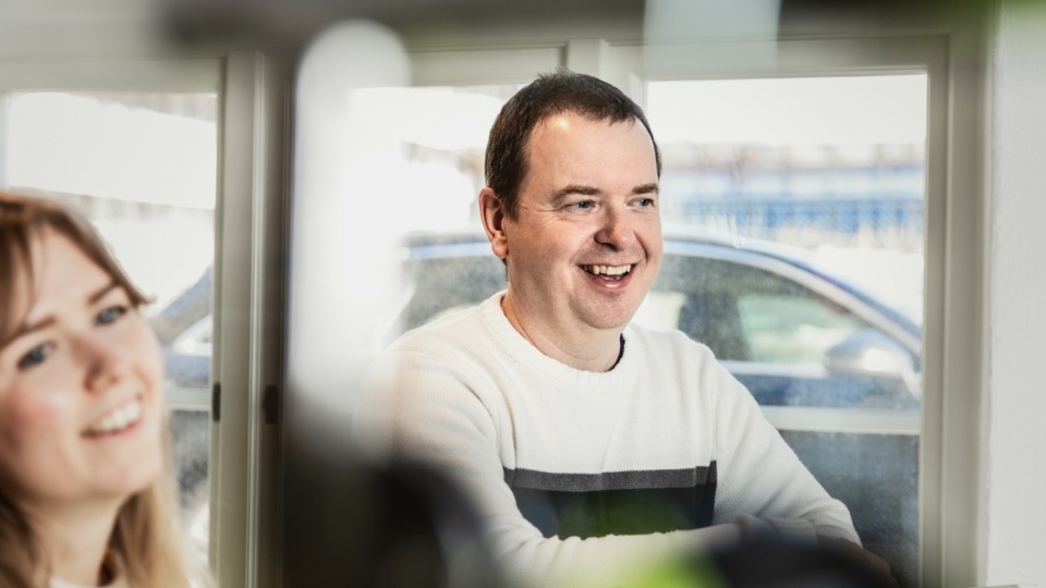 Två kollegor ler under ett möte vid ett ljust fönster