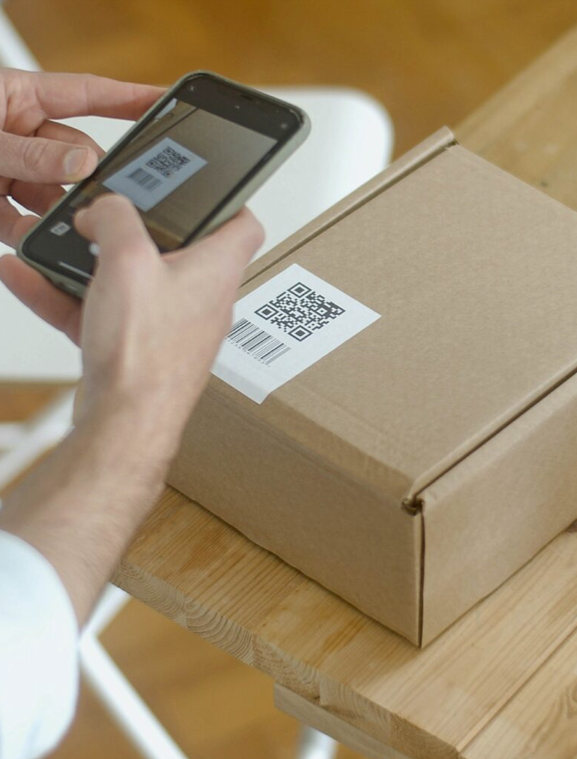 Person skannar QR-kod på kartongpaket med smartphone